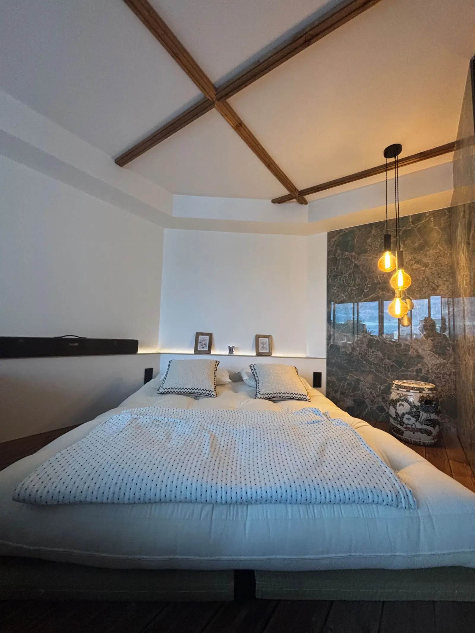 Le lit queen size sous les poutres claires, lampes suspendues